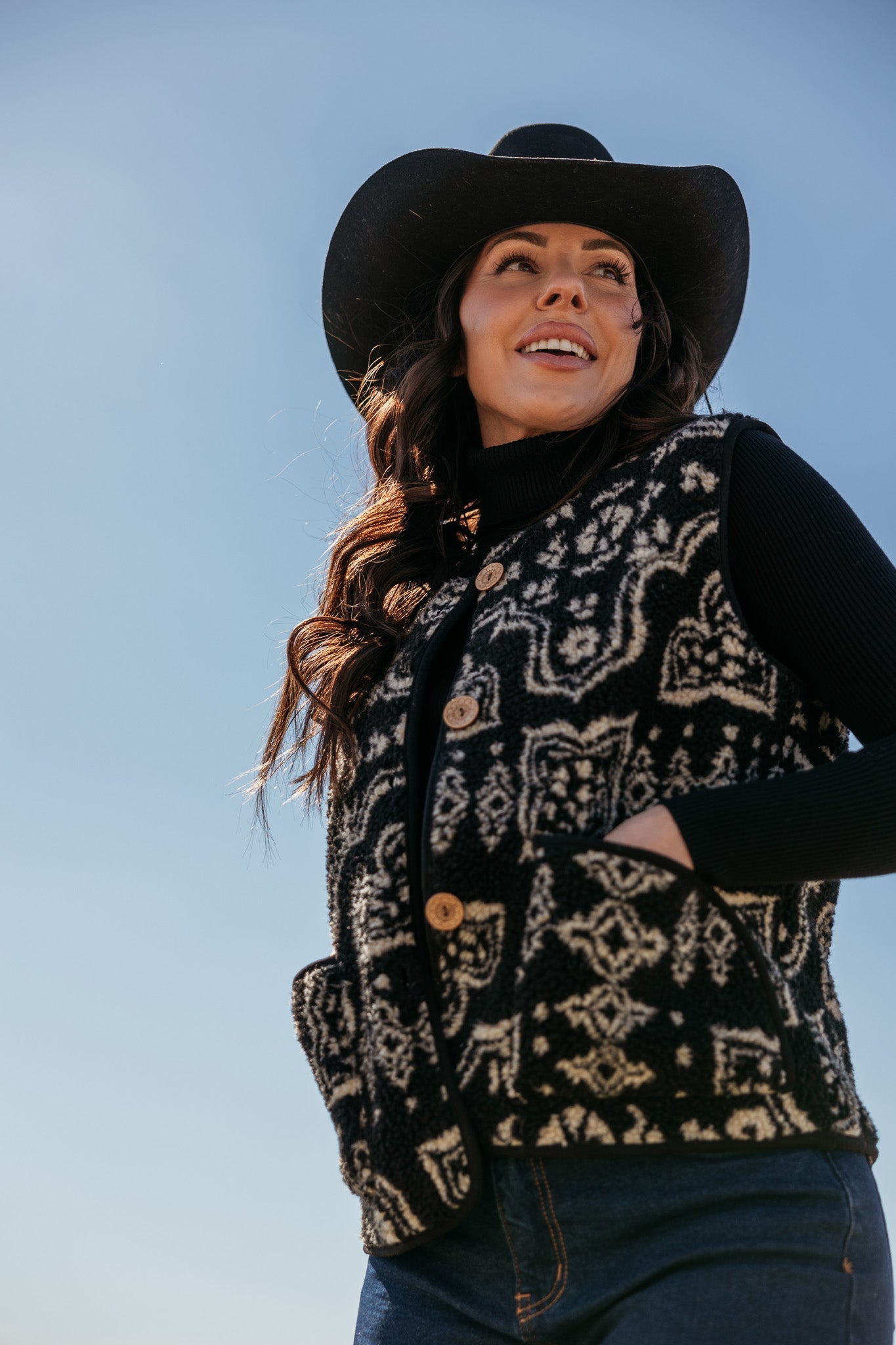 Woman in black cowboy hat and patterned western vest, western boho street style