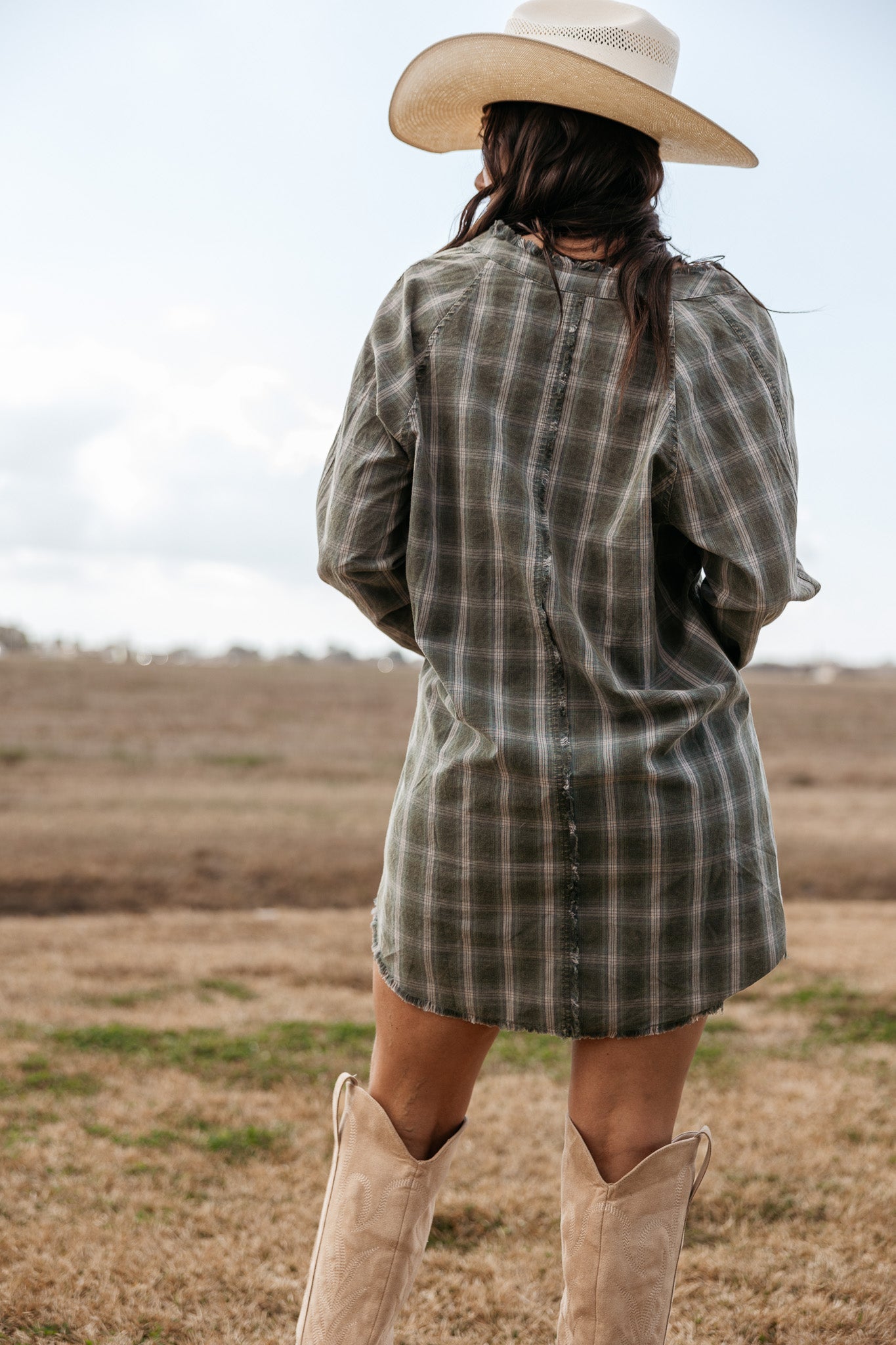Woman in plaid western dress, cowboy boots, and cowboy hat standing outdoors