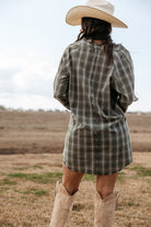 Woman in plaid western dress, cowboy boots, and cowboy hat standing outdoors