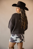 Woman in a western hat, chunky knit sweater, cow print skirt, and suede boots