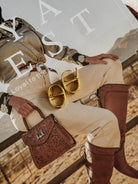 Gold western hoop earrings on magazine with cowgirl outfit, embroidered blouse, leather boots, tooled bag