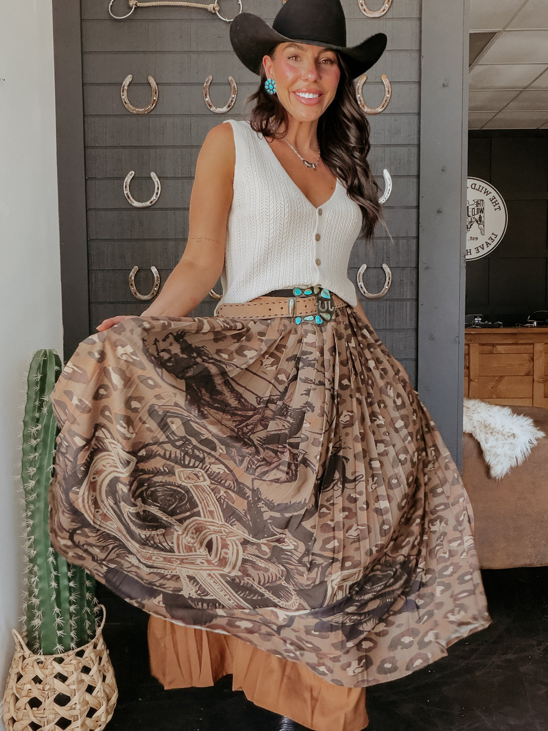 Woman in a stylish outfit with a patterned skirt and cowboy hat in a room with decorative elements.