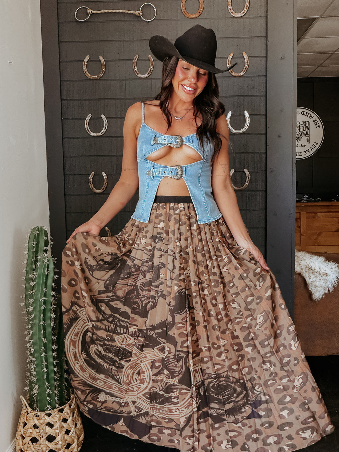 Woman in a cowboy hat and patterned dress standing next to a cactus plant.