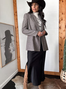 Woman in western boho outfit with cowboy hat, plaid blazer, turtleneck, long skirt, and boots