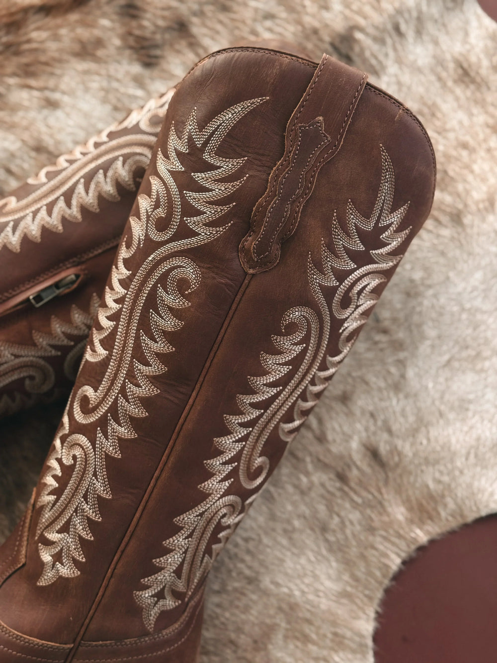 Brown leather boot with intricate white embroidery on a fur background