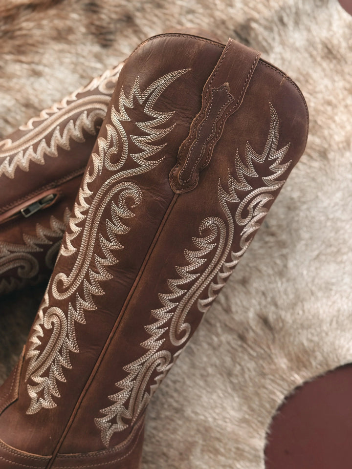 Brown leather boot with intricate white embroidery on a fur background