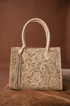 Western tooled leather handbag with floral design and braided handle on brown background