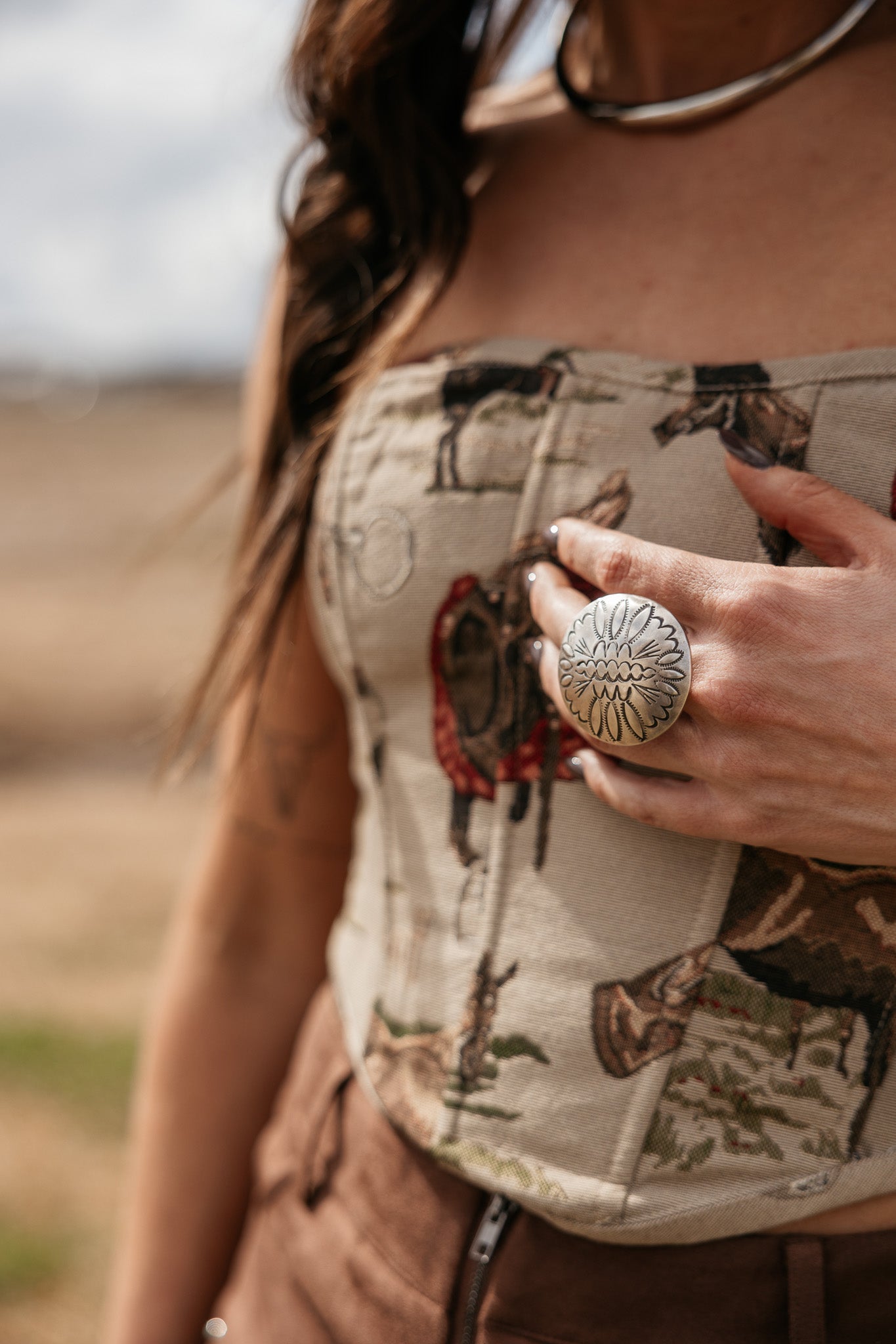 Woman wearing a western boho print corset top, statement silver ring, and brown suede pants