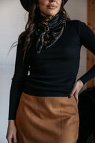 Woman wearing western boho outfit with black ribbed top, printed scarf, and tan suede skirt