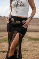 Woman in western boho rodeo tank top, black lace skirt with slit, concho belt, and jewelry