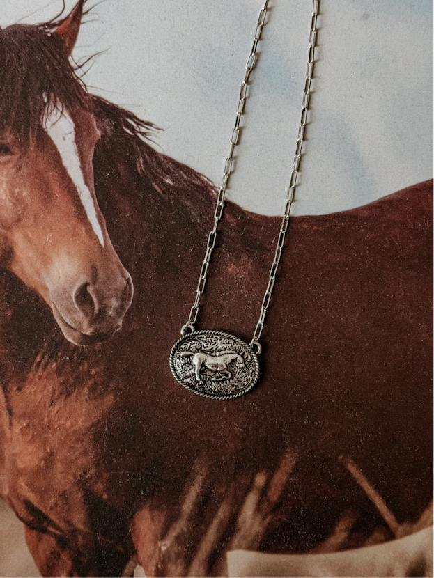 Western silver horse pendant necklace with engraved details on a horse-themed background.
