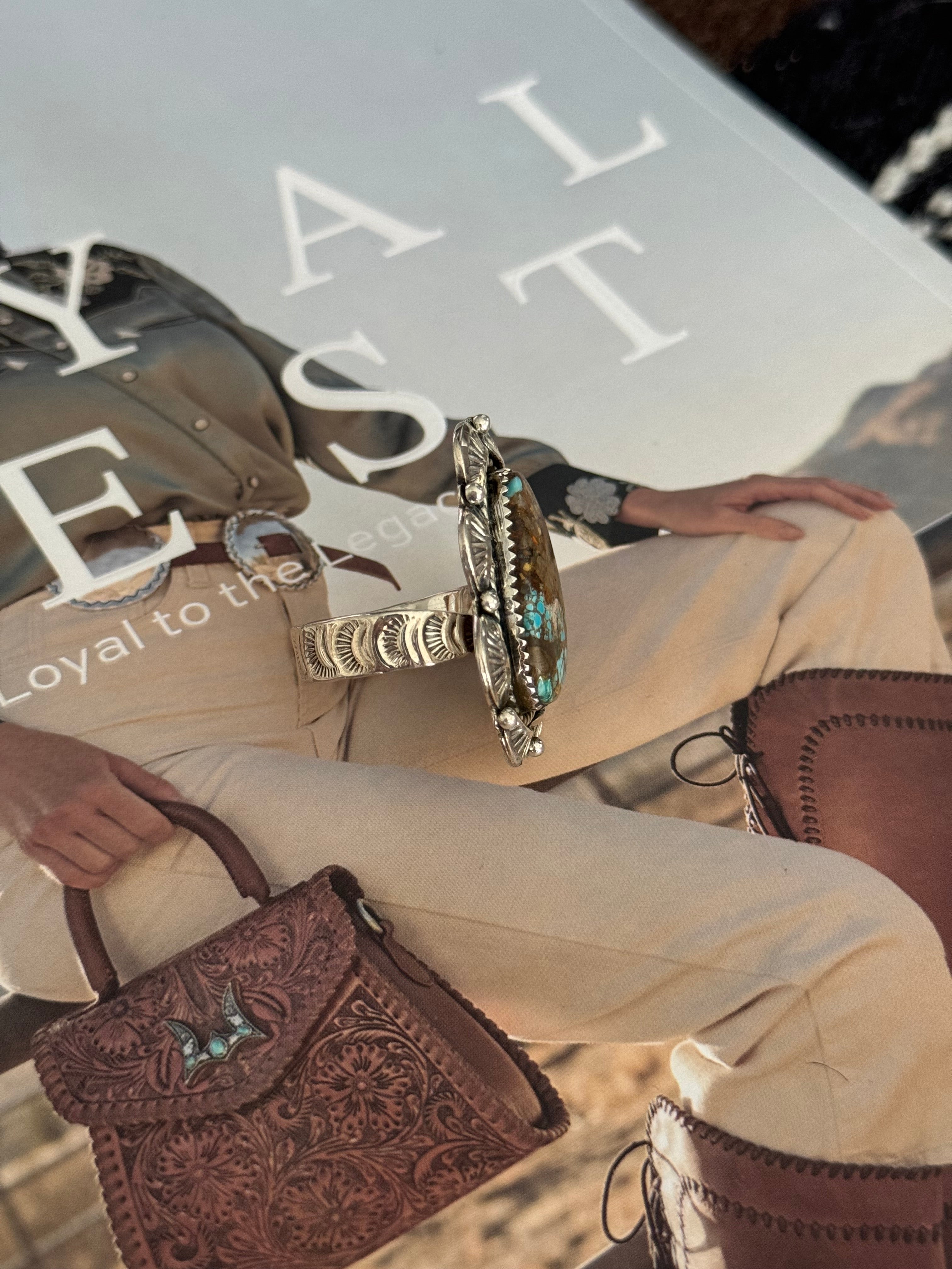 Western boho turquoise silver ring on embossed leather bag and cowgirl outfit background