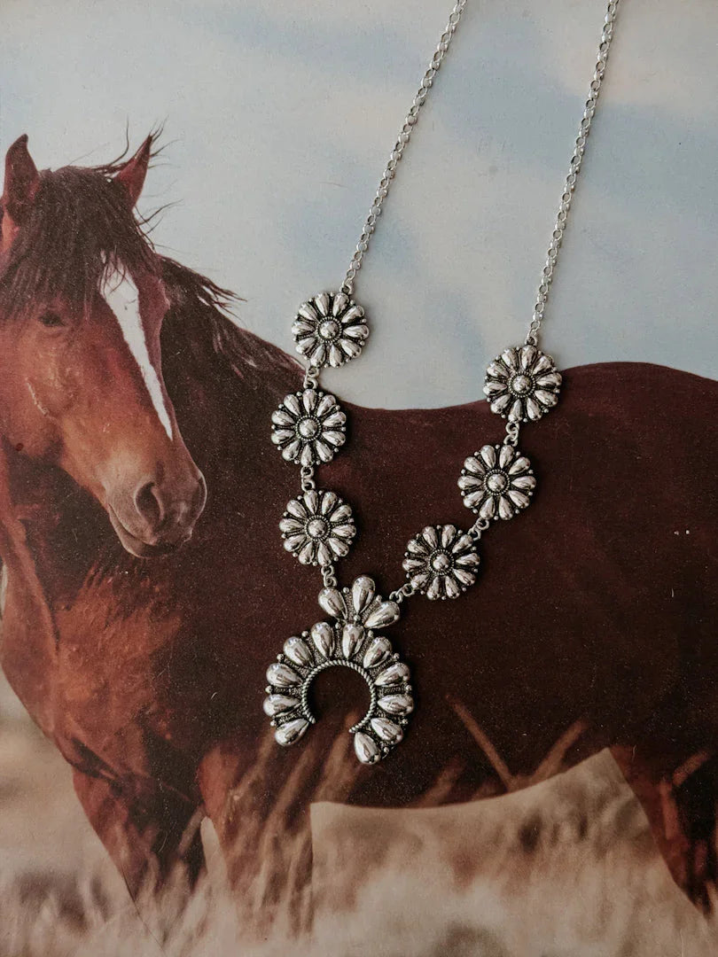 Silver western concho necklace with floral details displayed over a horse background