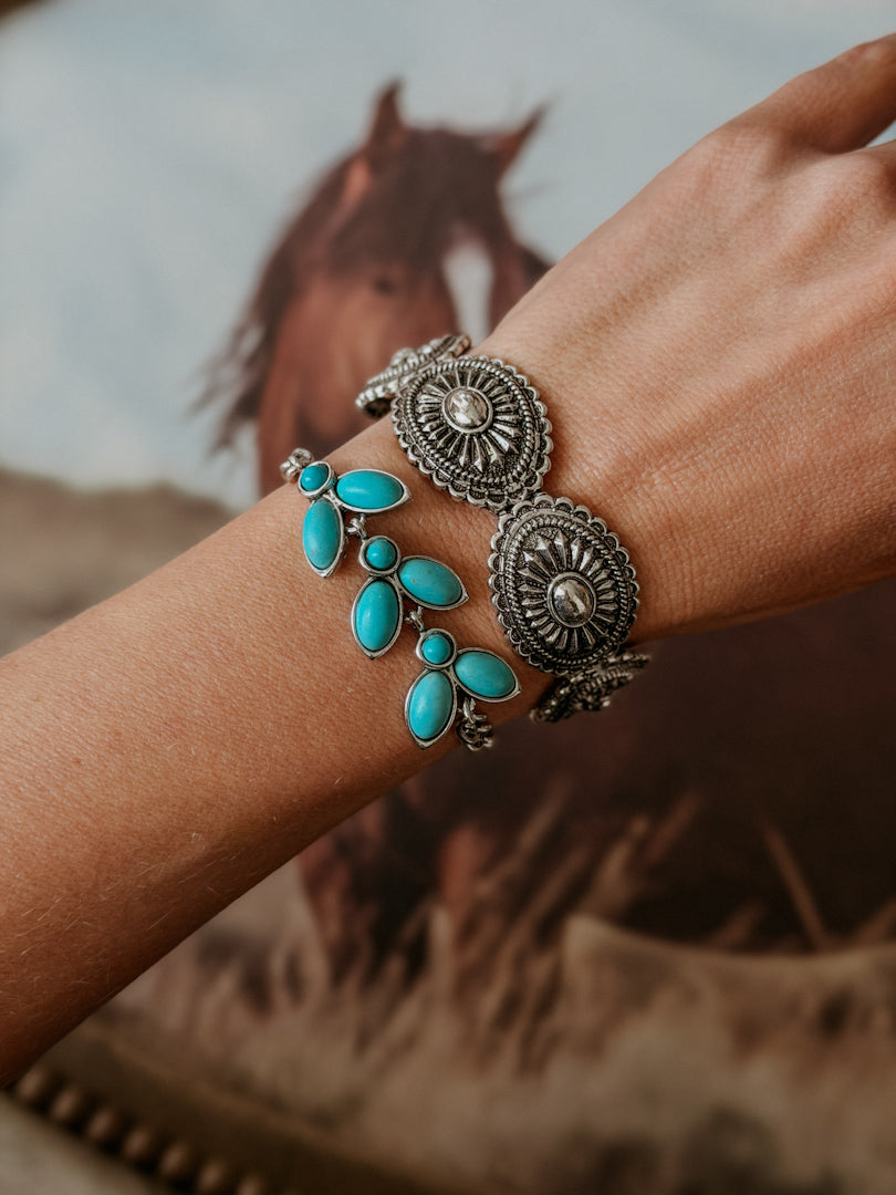 Western silver and turquoise bracelets on wrist with horse in background, boho jewelry style