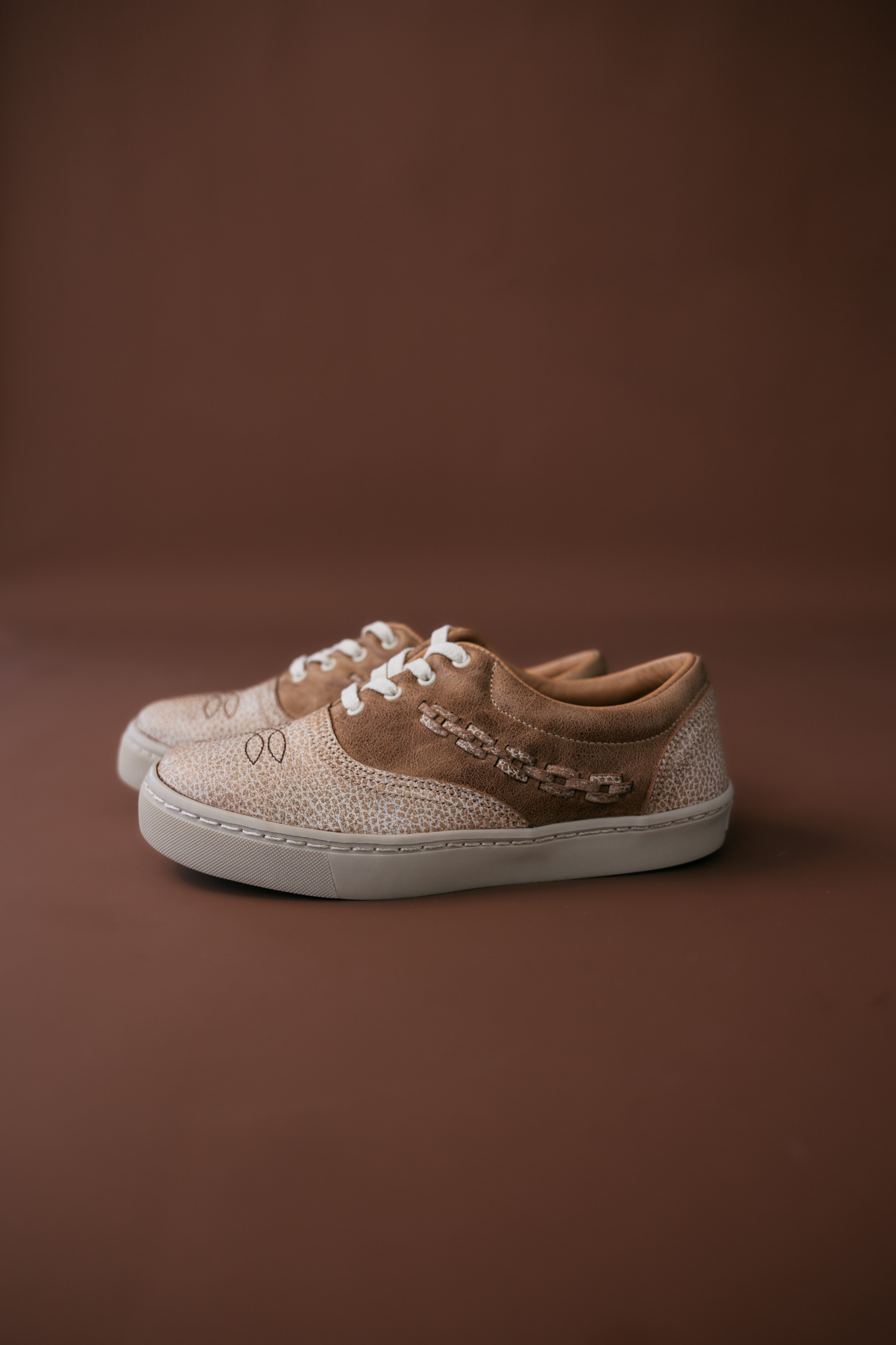 Western-inspired tan and white sneakers with textured details on brown background