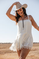 Woman in a white western boho dress and cowboy hat standing in a field