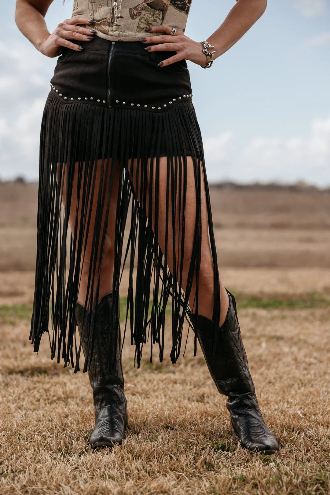 Woman wearing black fringe western skirt and cowboy boots in a country field