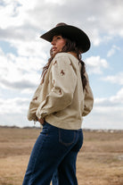 Woman in cowgirl hat, beige embroidered western jacket and blue jeans outdoors