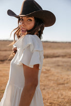 Woman in white ruffle dress and brown cowboy hat in a sunny western field
