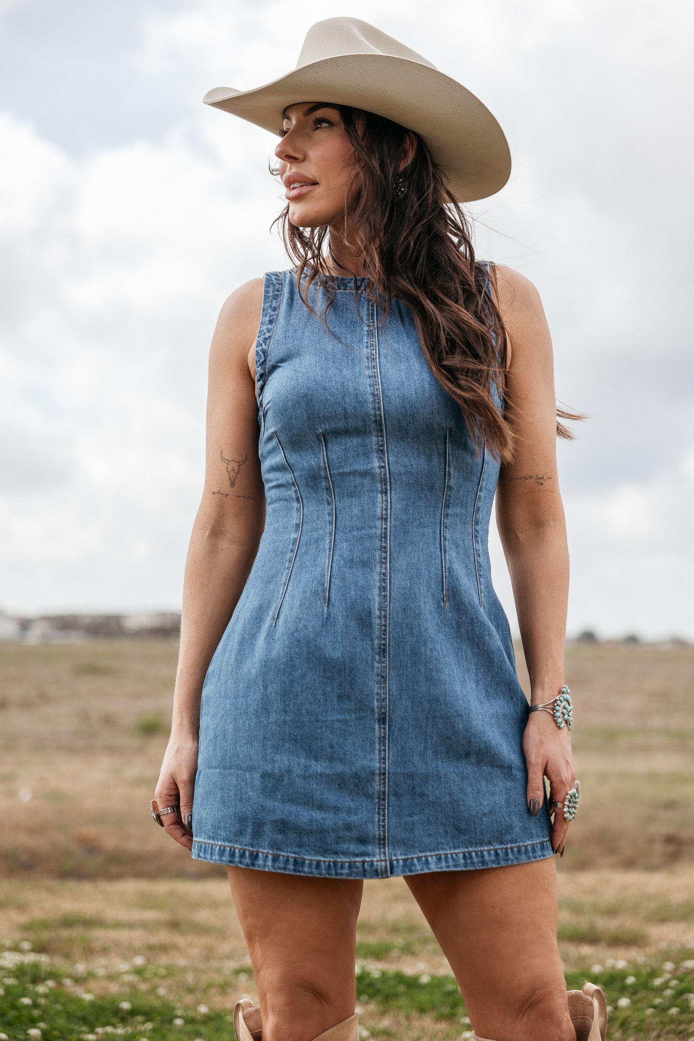 Woman in a denim western dress and cowboy hat standing outdoors in a field