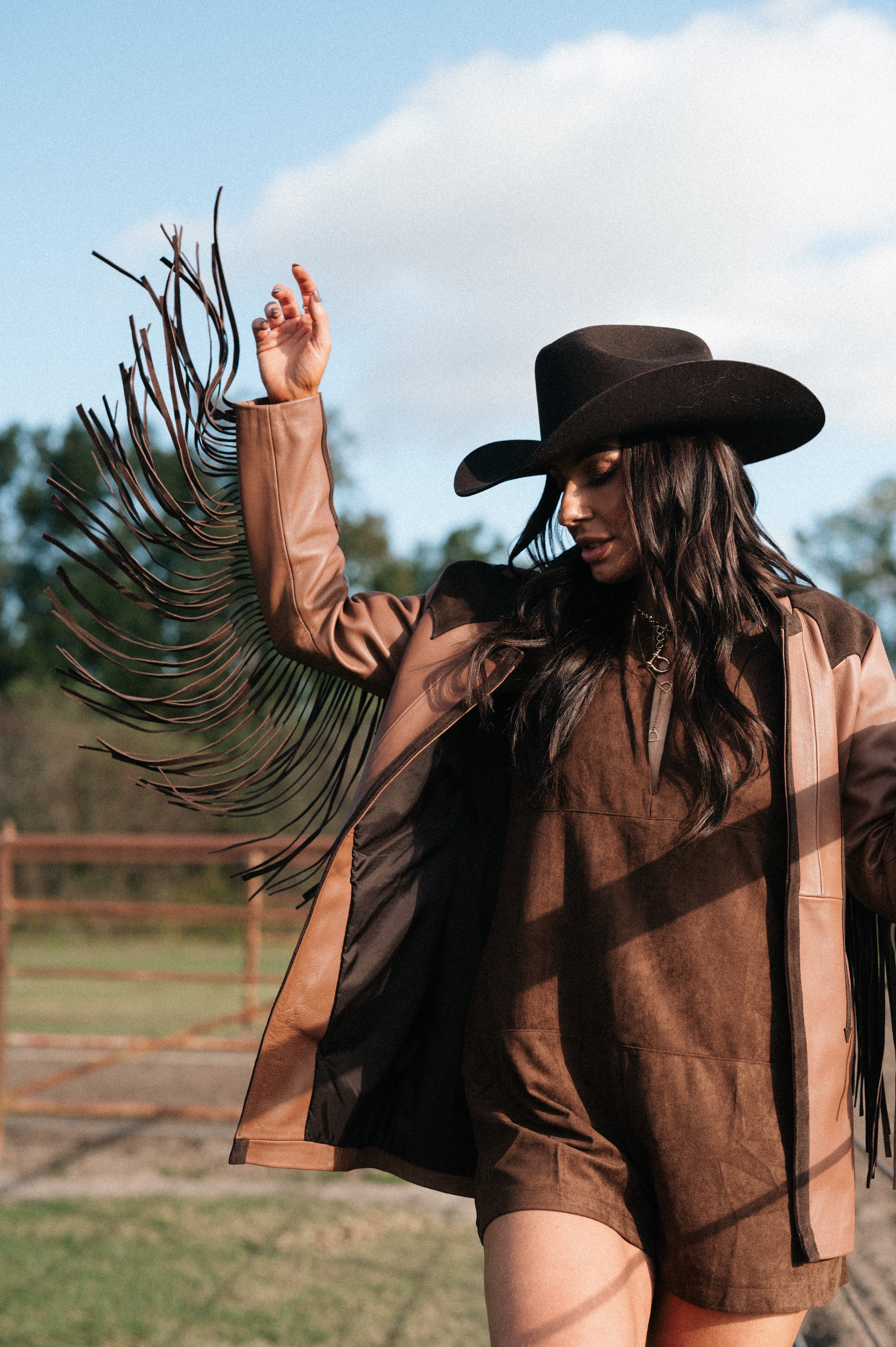 Woman in brown fringe western jacket and cowboy hat outdoors, boho cowgirl outfit