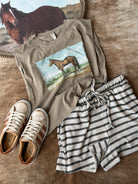 T-shirt with horse graphic, shorts, and sneakers on a wooden surface