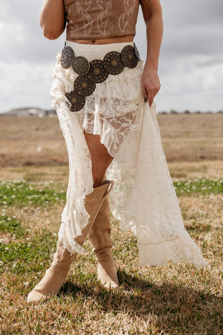 Woman in western lace skirt, concho belt, and tan cowboy boots outdoors