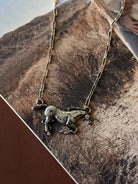 Thunderbird pendant chain necklace displayed on wooden slab with serape fabric underneath - The Wild J