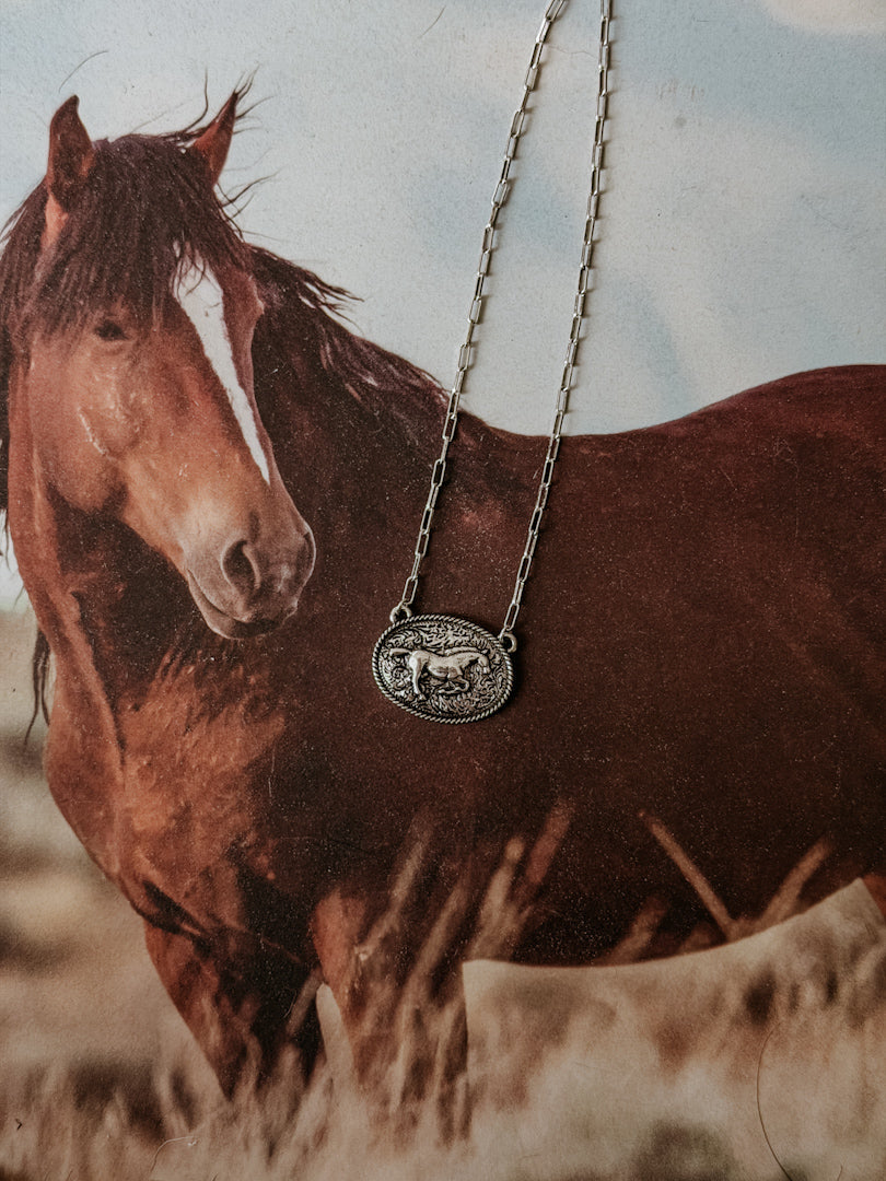 Western horse necklace with engraved pendant on a photo of a brown horse in a rustic setting