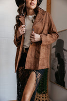 Woman in a brown suede western jacket, black lace skirt with thigh-high slit, and wide-brim hat