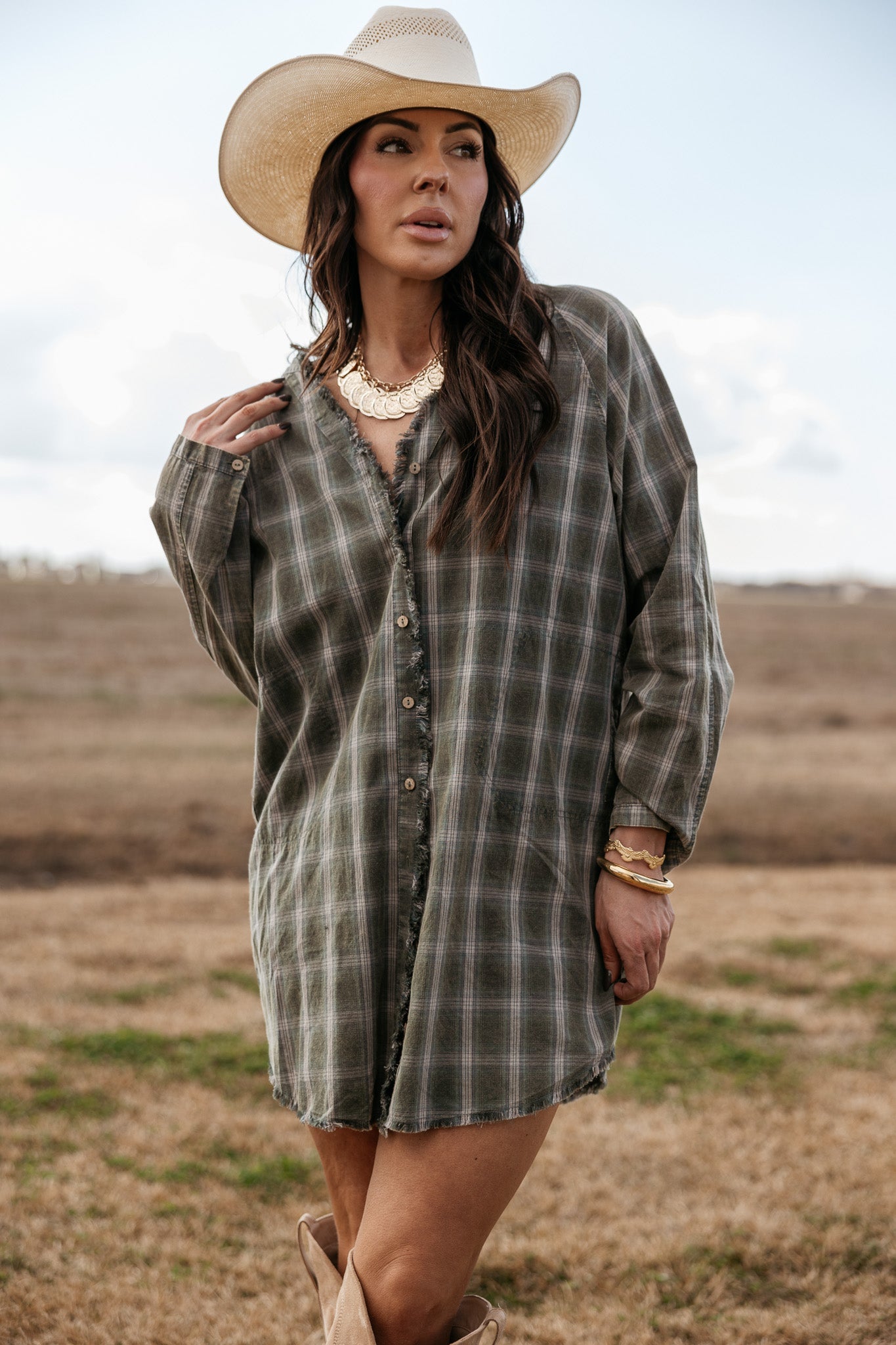 Woman in a plaid western shirt dress, cowboy hat, and statement jewelry outdoors