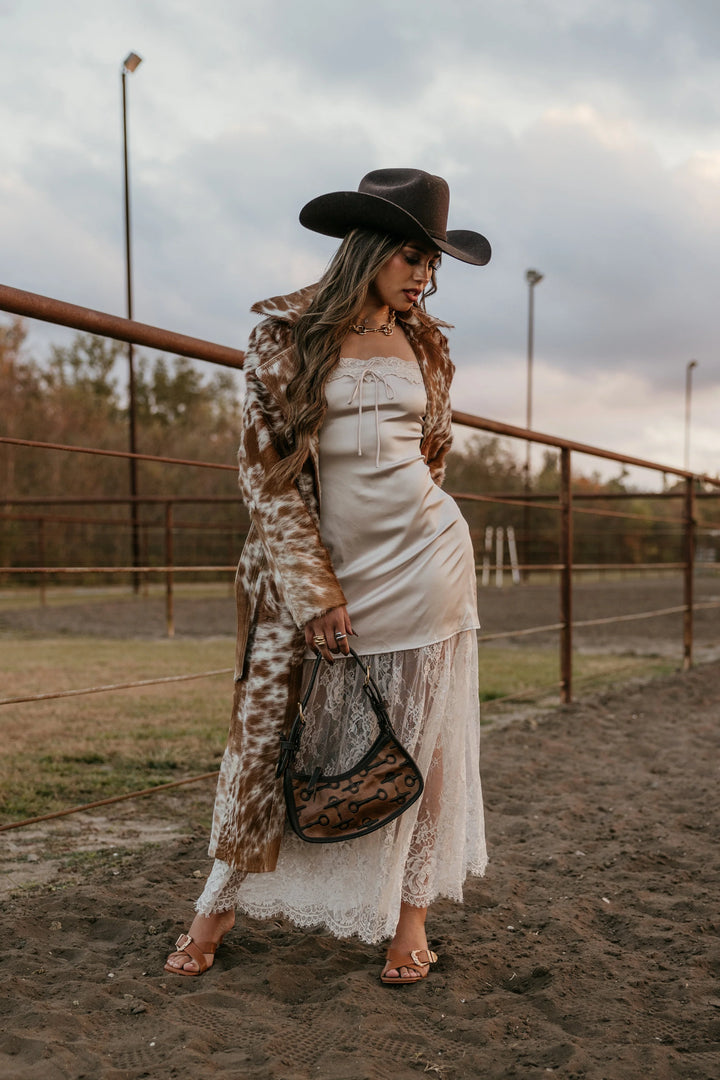 Woman in a white dress and brown hat standing in an outdoor setting with a cloudy sky.