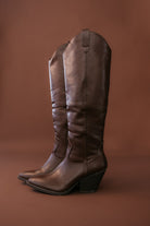 Pair of brown leather western cowgirl boots with a block heel on a brown background