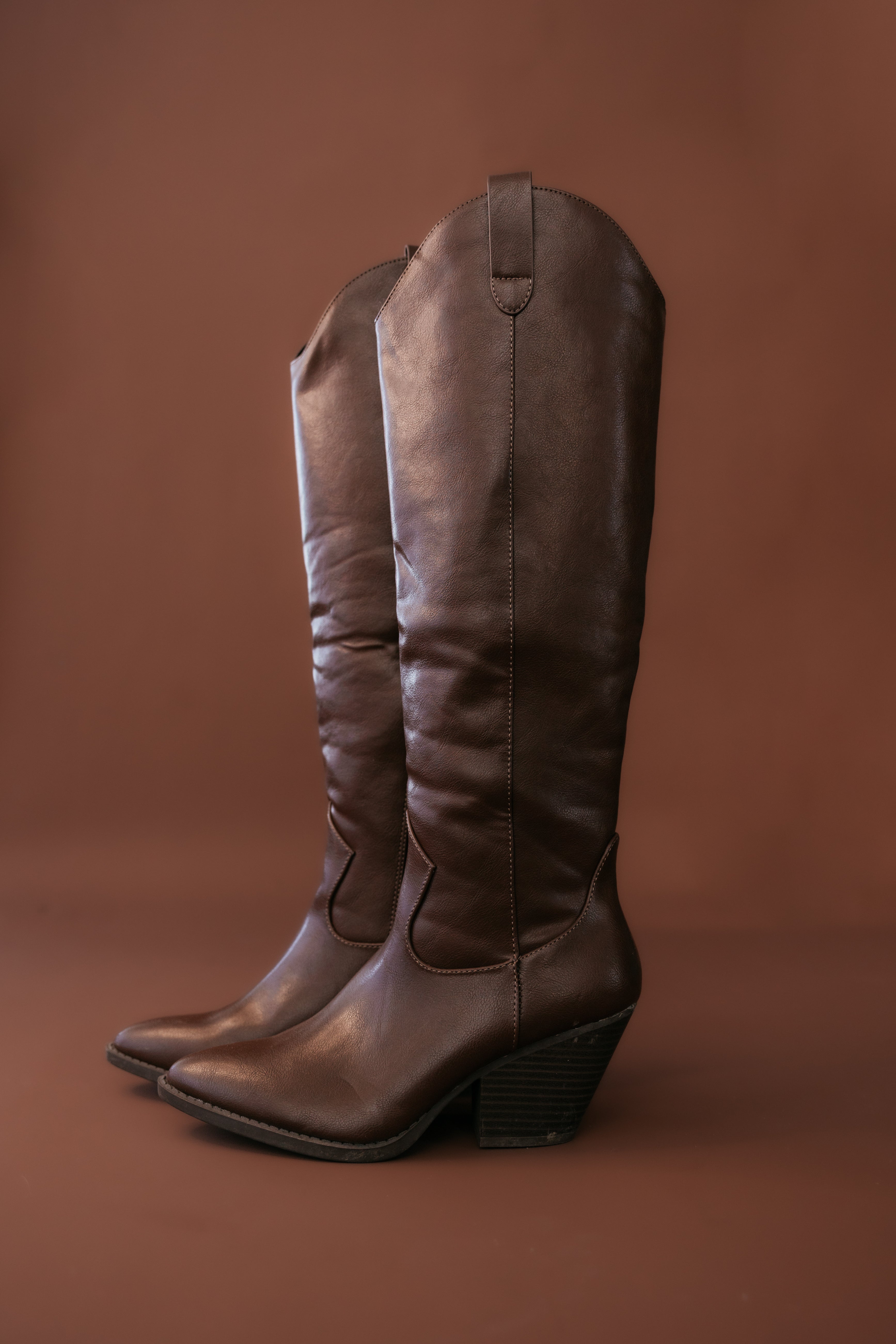 Pair of brown leather western cowgirl boots with a block heel on a brown background