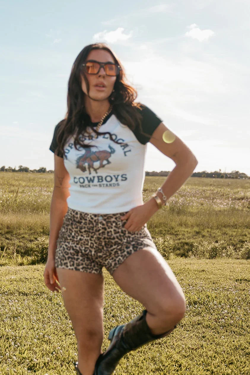 Woman wearing a 'Cowboys' t-shirt and leopard print shorts in an open field.