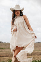 Woman in cream western dress and cowboy hat posing outdoors in boho cowgirl style