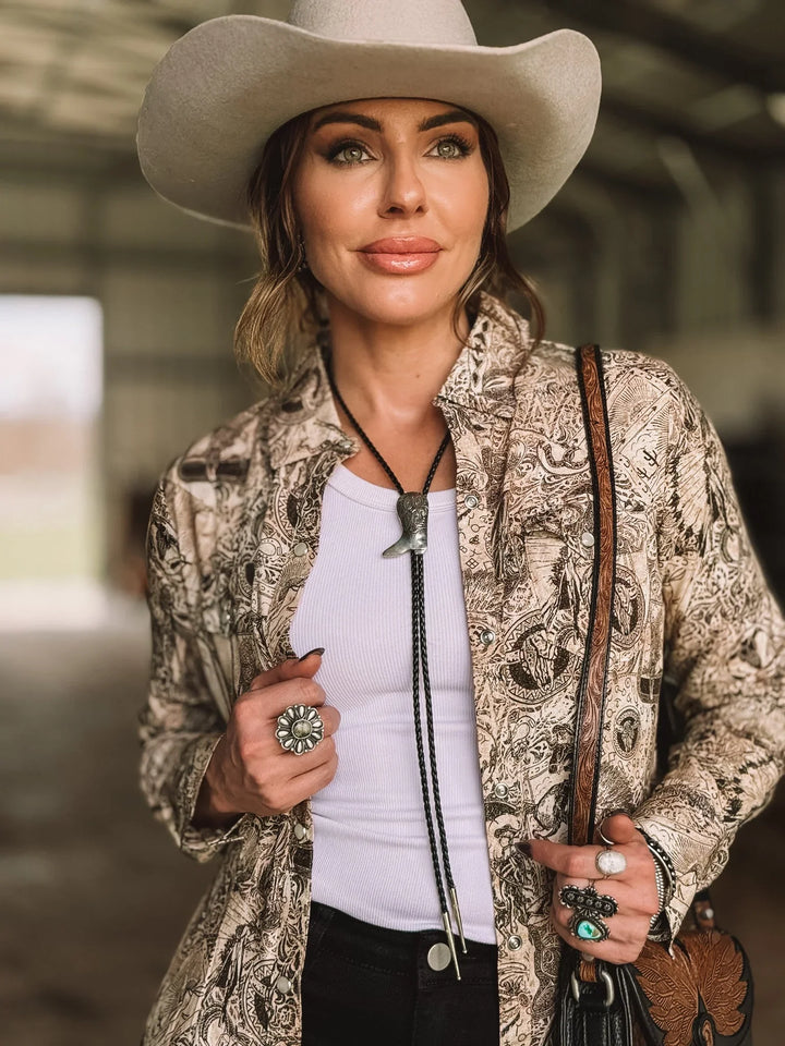 Woman in a white cowboy hat, western bolo tie, boho print shirt, and turquoise rings