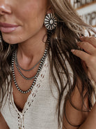 Woman wearing western boho silver statement earrings, layered necklaces, cream crochet top