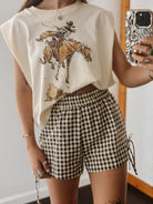 Person wearing a graphic t-shirt with a horse and rider design and checkered shorts.