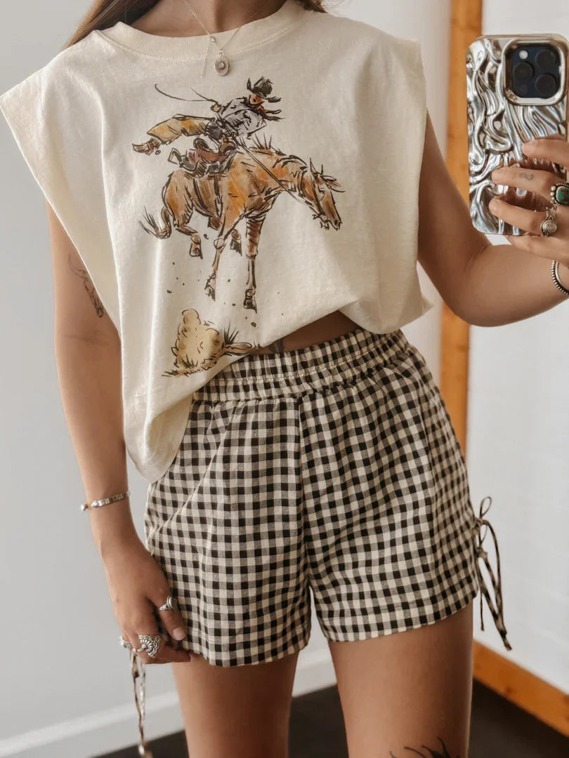 Person wearing a graphic t-shirt with a horse and rider design and checkered shorts.