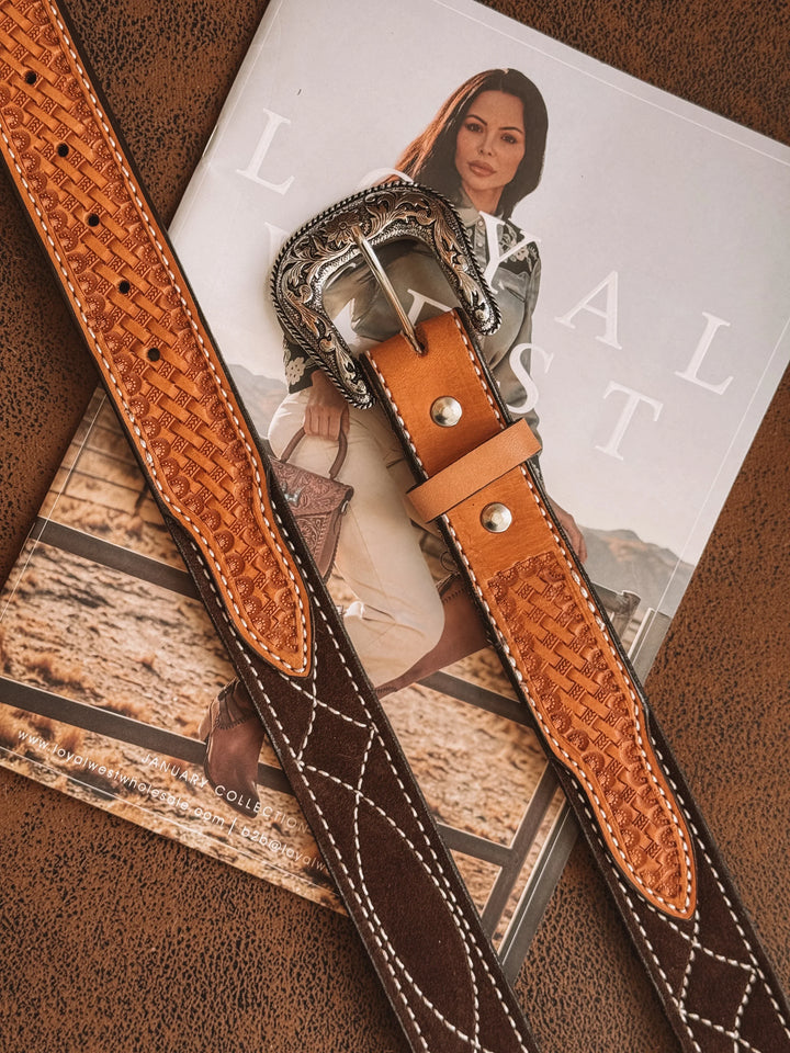 Tooled leather western belt with ornate silver buckle on a magazine featuring cowgirl fashion.