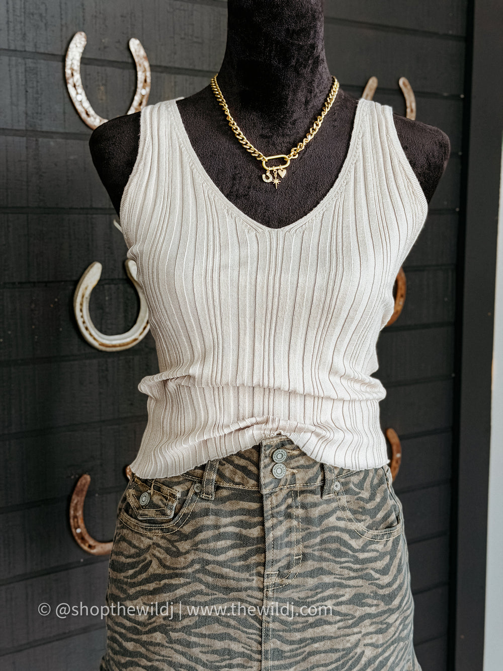 Mannequin wearing a white ribbed tank top and zebra print skort with gold necklace against a dark background.