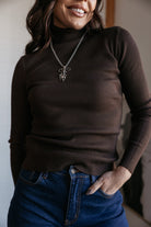 Woman wearing a ribbed brown turtleneck, western pendant necklace, and high-waisted jeans