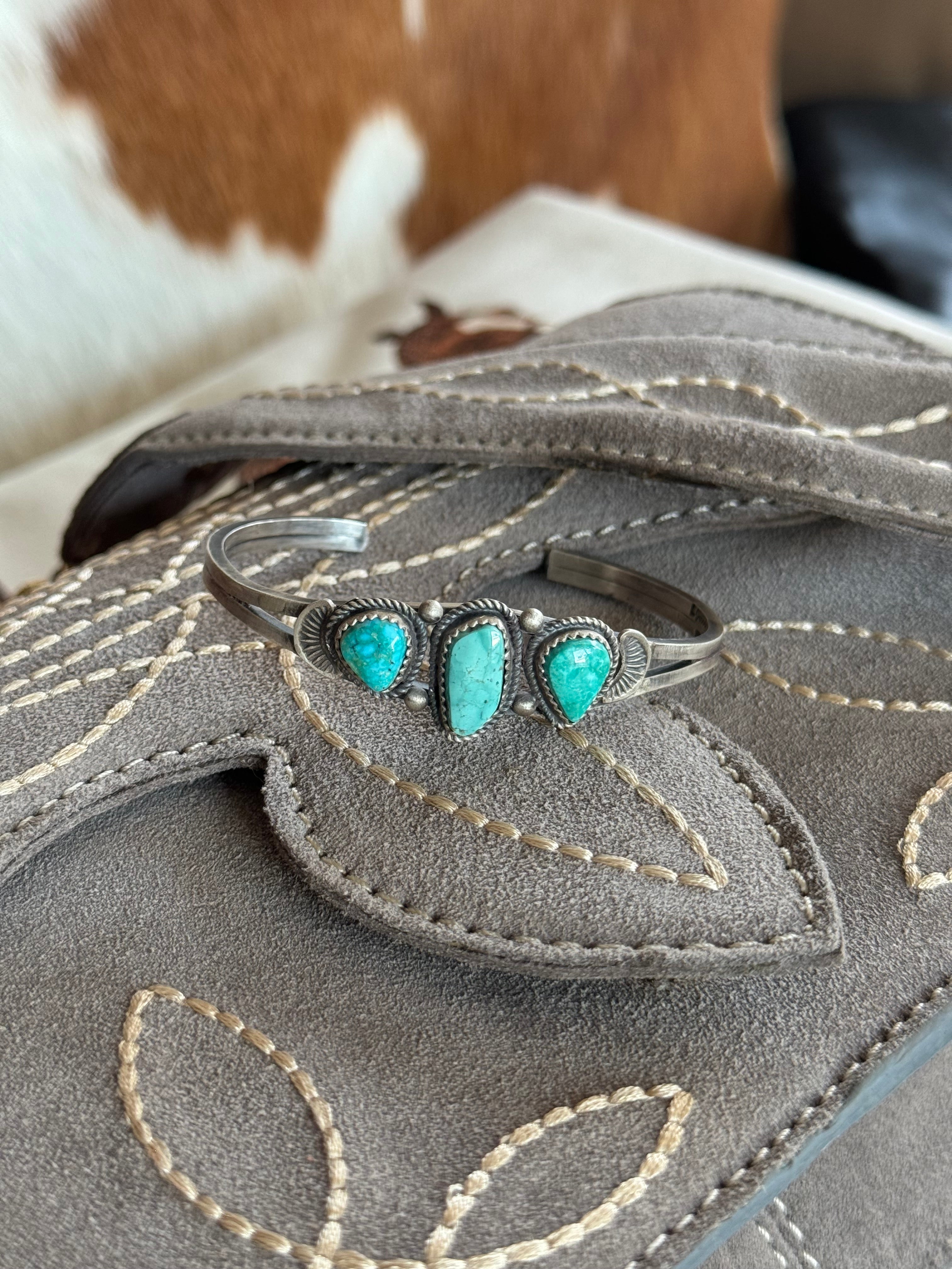 Western turquoise cuff bracelet with silver setting on embroidered suede bag, cowhide background