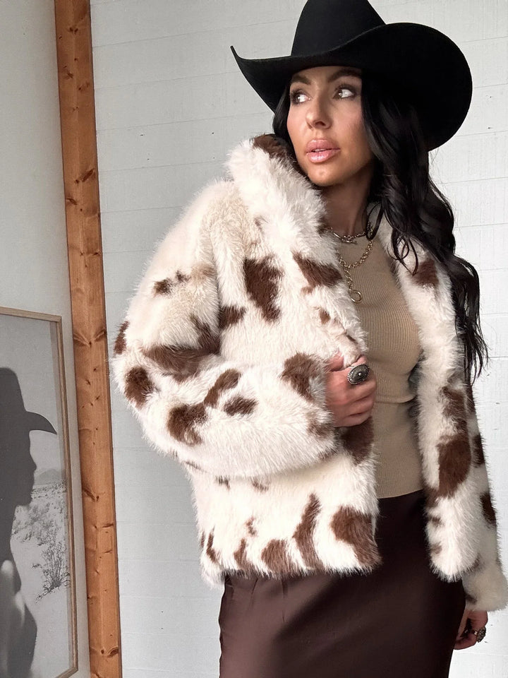 Woman wearing a cow print fur coat and black hat indoors.