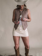 Woman in cowgirl hat wearing western vest, white mini skirt, cowboy boots, and boho jewelry