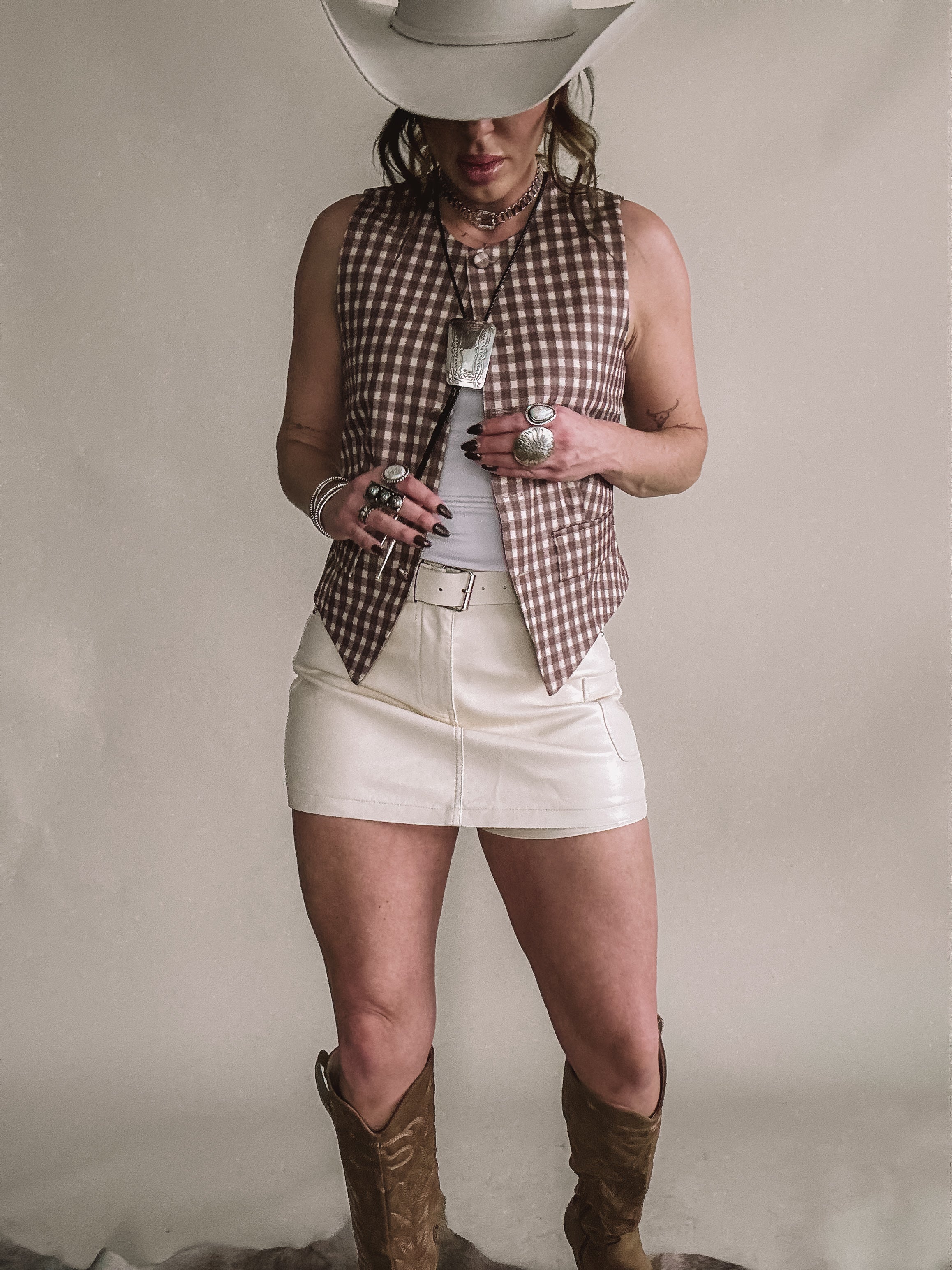 Woman in cowgirl hat wearing western vest, white mini skirt, cowboy boots, and boho jewelry