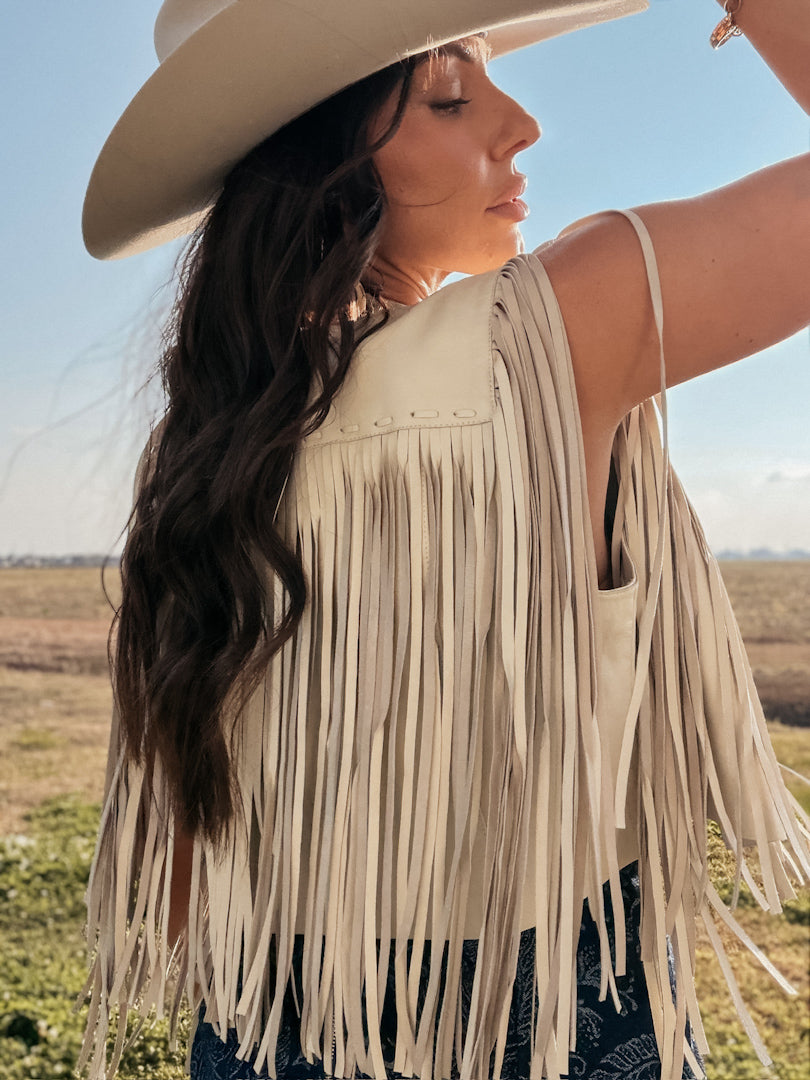 Woman in cream fringe vest and cowboy hat, western boho style, outdoor setting