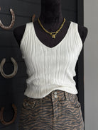 Mannequin wearing a white ribbed tank top and zebra print pants with a gold necklace against a dark background.