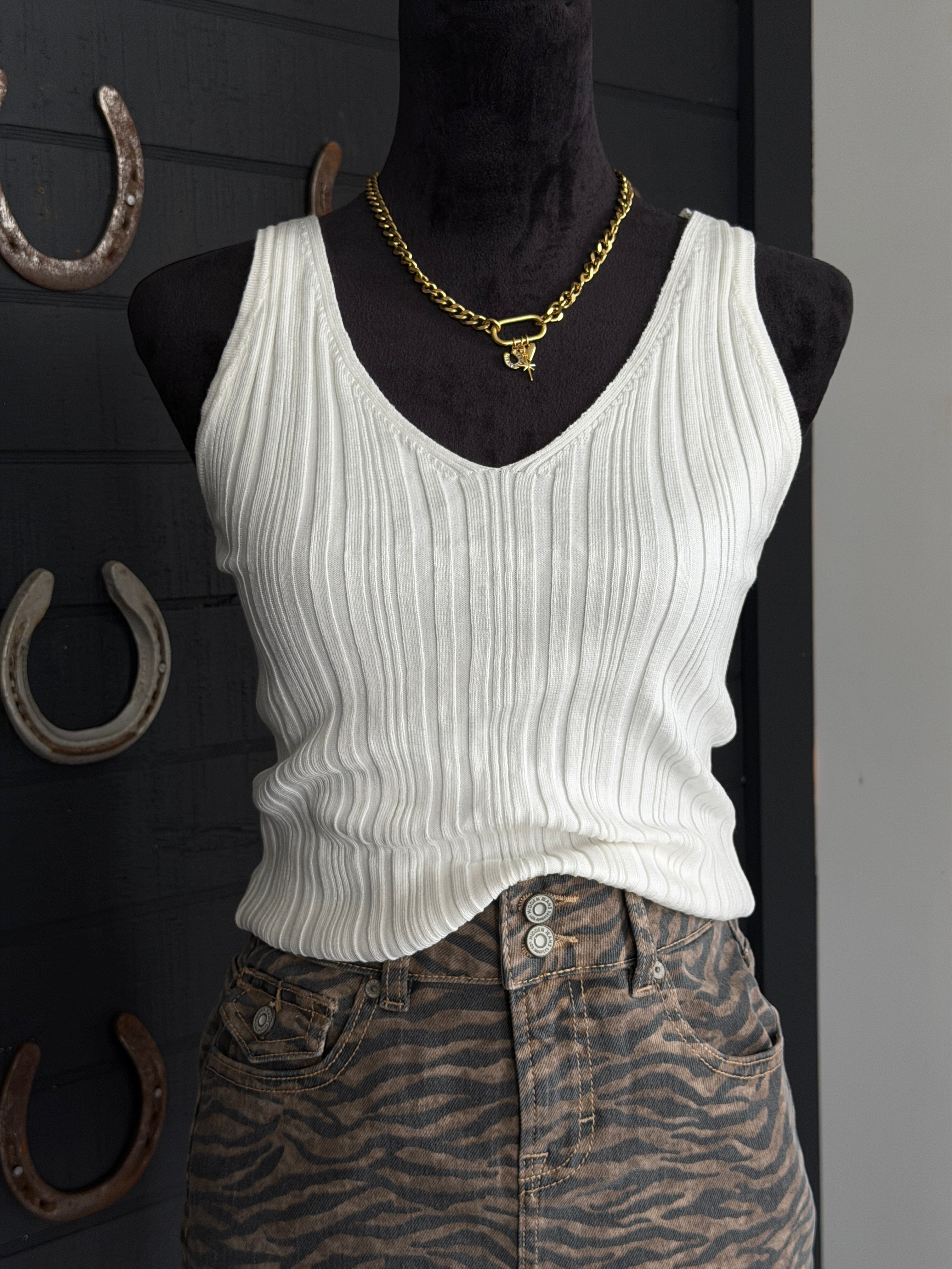 Mannequin wearing a white ribbed tank top and zebra print pants with a gold necklace against a dark background.